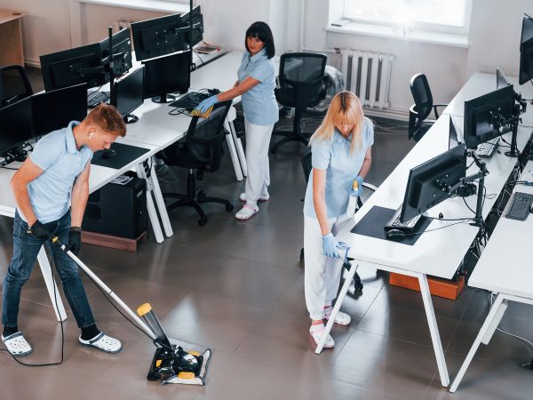 Cleans floor. Group of workers clean modern office together at daytime.
